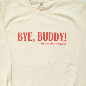 May include: A cream colored sweatshirt with the text "BYE, BUDDY! hope you find your dad *" in red.