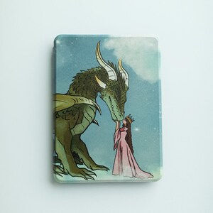 Könnte beinhalten: Ein rechteckiges Produkt mit einer Fantasy-Illustration. Ein grüner Drache mit goldenen Hörnern und Flügeln schmust mit einer Frau in einem rosa Kleid und Krone. Der Hintergrund ist ein blauer Himmel mit Wolken und Sternen.