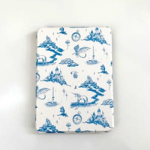 May include: White rectangular case with a blue fantasy pattern. The design includes castles, dragons, unicorns, compasses, and other whimsical elements. The case has rounded corners and a smooth surface.