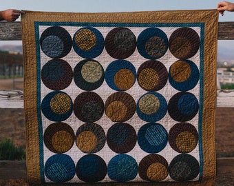 May include: A quilt with a geometric pattern of overlapping circles in shades of brown, blue, and gold. The circles are arranged in a grid pattern on a white background.