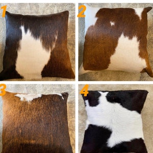 May include: Four square cowhide throw pillows with different color patterns. The pillows are brown and white, brown and white, brown and white, and black and white.