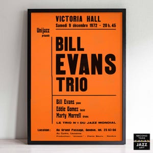 May include: Framed vintage poster with an orange background and black text. The poster advertises a performance by the Bill Evans Trio at Victoria Hall on December 9, 1972. Includes the names of the musicians and the location.