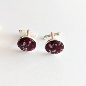May include: A pair of silver cufflinks with round, dark purple resin insets containing silver flakes.