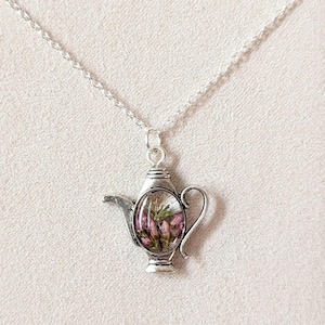 May include: A silver necklace with a teapot pendant. The teapot is filled with dried pink and white flowers.