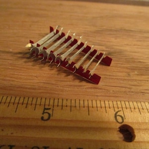 May include: A set of miniature wrenches with red handles arranged in a triangular shape on a wooden surface. The wrenches are made of silver metal and have a shiny finish.