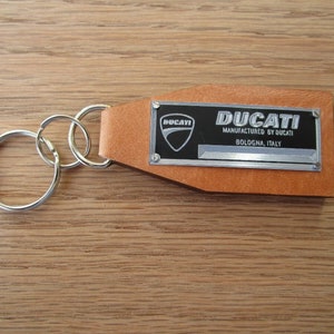 May include: A brown leather keychain with a silver metal tag that says "DUCATI MANUFACTURED BY DUCATI BOLOGNA, ITALY".