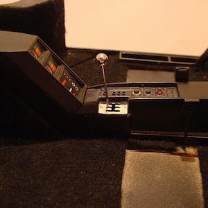 May include: A black car interior with a black leather dashboard and a silver gear shifter. The dashboard has a series of buttons and a digital display.