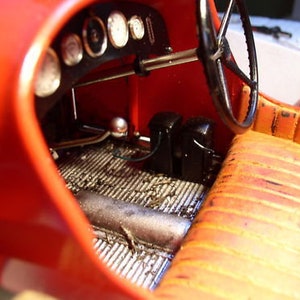 Może przedstawiać: Zbliżenie wnętrza czerwonego samochodu vintage. Samochód ma czarną kierownicę, czarną deskę rozdzielczą z wskaźnikami i czarne skórzane siedzenie. Wnętrze jest szczegółowo wykonane z teksturalną podłogą i czarną metalową dźwignią zmiany biegów.