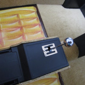 May include: A close-up of a black car interior with a silver gear shifter and a brown carpet. The carpet has a yellow and orange patterned design.