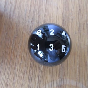 Op de afbeelding: Zwarte versnellingspookknop met witte cijfers 1, 2, 3, 4, 5 en R.