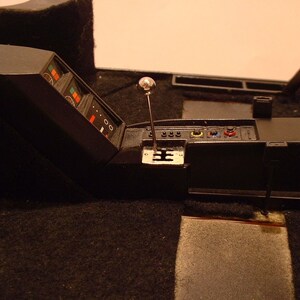 May include: A black car interior with a silver gear shifter and a black dashboard with multiple buttons and a digital display.