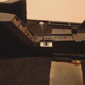 Peut inclure: Intérieur de modèle de voiture détaillé, avec un tableau de bord noir avec jauges et commandes. Un levier de vitesses chromé et un plancher recouvert de moquette noire sont également visibles. Le modèle est sur fond neutre.