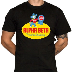 May include: Black t-shirt with a yellow and red logo featuring a cartoon cowboy holding a blue ribbon with the word "ACME" on it. The logo also includes the text "ALPHA BETA First in Quality".