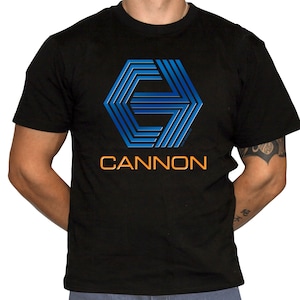 May include: Black t-shirt with a blue and white geometric logo and the word "CANNON" in orange letters.