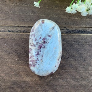May include: A smooth, oval-shaped, polished stone with a white base and scattered red and purple inclusions.