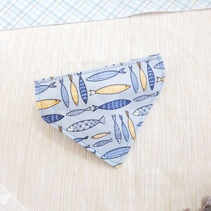 May include: A light blue bandana with a pattern of yellow and blue fish. The bandana is triangular in shape and has a white background.