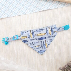 May include: A light blue cat collar with a bell and a matching bandana featuring a pattern of yellow and blue fish.