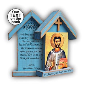 Op de afbeelding: Een lichtblauw houten huisvormig bord met een icoon van de heilige Augustinus met een gouden aureool. De voet is gegraveerd met "St. Augustyne, Pray For Us." Het achterpaneel toont een verjaardagsboodschap en een label "Your TEXT on the back".