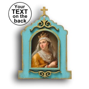 Puede incluir: Un retrato enmarcado de una mujer con corona y velo blanco, enmarcado en un marco turquesa desgastado con detalles dorados. El marco tiene una cruz en la parte superior y el texto "Your TEXT on the back" en un círculo.