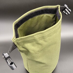 May include: Olive green pouch with a black velcro closure and a black plastic clip. The pouch is made of a durable fabric and has a drawstring closure. The pouch is designed to hold small items.