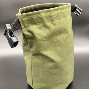 May include: Olive green pouch with a black strap and buckle closure. The bag is made of a durable fabric and has a rectangular shape with a folded top. The interior is lined with black material. The bag is designed for carrying small items.