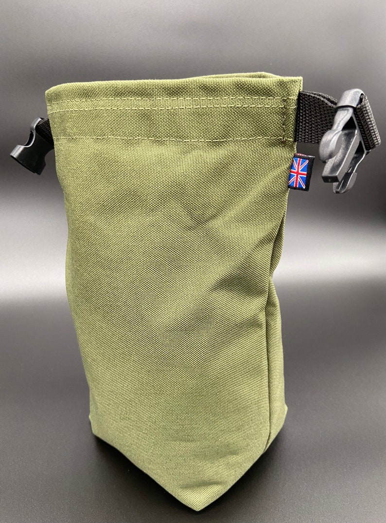 May include: Olive green drawstring bag with black plastic buckles and a black strap. The bag has a small Union Jack tag. The bag is made of a durable, textured fabric.