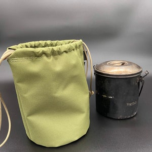 May include: An olive green drawstring bag with tan drawstrings next to a black metal container with a silver lid. The bag is made of a durable fabric and is designed to hold items. The container has a handle and is likely used for cooking or storage.