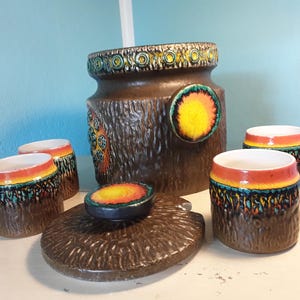 Könnte beinhalten: Eine braune Keramik-Bowle mit Deckel und sechs passenden Bechern. Die Schüssel und die Becher haben eine Holzmaserung und farbenfrohe geometrische Muster.