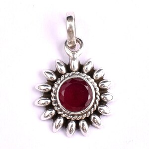 May include: A silver pendant with a red gemstone in the center, surrounded by a silver sunburst design.