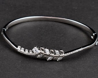 May include: A silver bangle bracelet featuring a delicate leaf design with clear cubic zirconia stones.