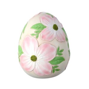 May include: A white ceramic egg-shaped ornament decorated with pink and green flowers. The flowers are raised and have a realistic appearance.