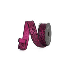 May include: A roll of magenta ribbon with black glitter accents. The ribbon is partially unrolled, displaying its texture and design. The spool is dark gray with a label.