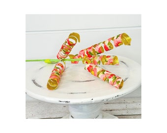 May include: Four gold and pink floral ribbon curls on a white cake stand. The ribbon is curled and twisted, creating a decorative element.