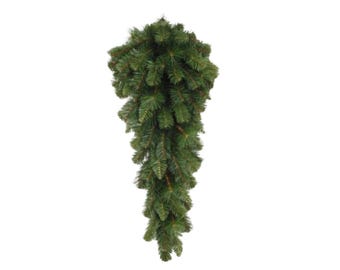 May include: A green artificial Christmas swag with a teardrop shape. The swag is made of faux pine needles and is designed for holiday decorating. The swag is displayed against a white background.