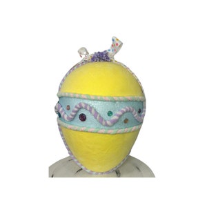 May include: A large yellow Easter egg with a blue and purple ribbon and a light pink and green rope design. The egg is decorated with colorful glitter and gems.