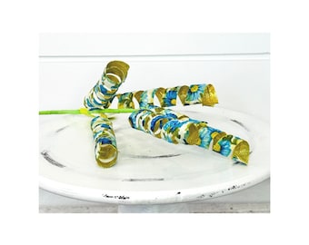 May include: Three gold and white floral ribbon curls on a white cake stand. The ribbon is curled and has a gold metallic finish.