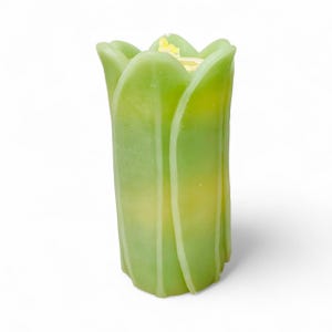 May include: A green and yellow tulip-shaped candle. The candle has a layered design with a light green exterior and a yellow interior. The candle is standing upright against a white background.