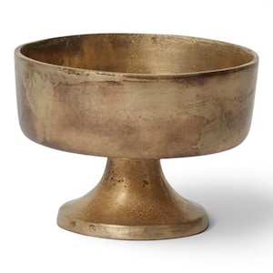 May include: A gold-colored, pedestal bowl with a wide, shallow basin. The bowl has a textured, aged appearance, with variations in the gold tone. The base is a rounded, flared shape, providing stability. This decorative bowl is suitable for various uses.