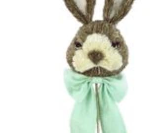 May include: A brown and white bunny head with long ears, a brown nose, and a green bow. The bunny head is attached to a stick.