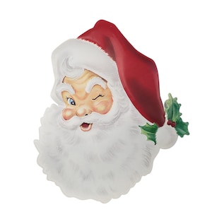 May include: A die-cut paper decoration featuring a winking Santa Claus head with a thick white beard, rosy cheeks, and a red hat trimmed with white fur. A small sprig of green holly leaves with two red berries is attached to the side of the hat.
