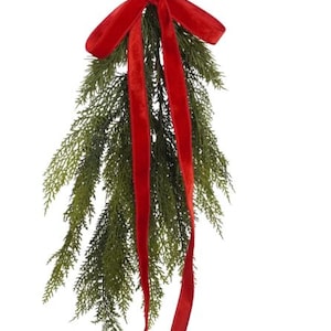 May include: A decorative Christmas sprig featuring green foliage and a vibrant red velvet bow. The bow is tied at the top and has long, flowing ribbons. The sprig is perfect for holiday decor.
