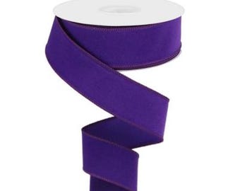 May include: A spool of purple velvet ribbon with a burgundy edge. The ribbon is wound around a white spool.