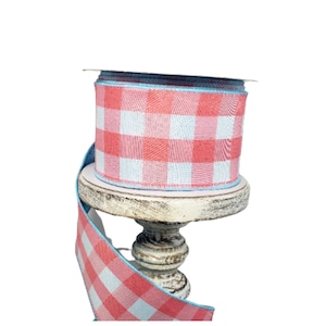 May include: A roll of pink and white gingham ribbon with a blue edge. The ribbon is wrapped around a wooden spool.