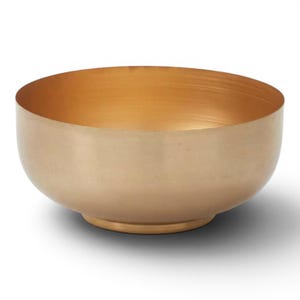 May include: A gold-colored metal bowl with a rounded shape and a slightly flared rim. The interior of the bowl has a brighter gold finish, contrasting with the exterior. The bowl sits on a small, circular base.