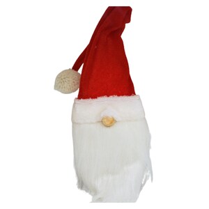 May include: A red and white gnome hat with a white fur beard and a wooden nose. The hat has a white pom-pom on top.