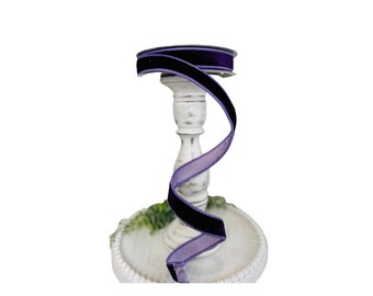 May include: A spool of purple velvet ribbon with a satin edge. The ribbon is wrapped around a white pedestal.