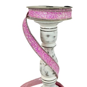 Puede incluir: Cinta de purpurina rosa sobre un fondo blanco. La cinta está envuelta alrededor de un candelero blanco.