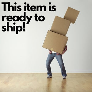 May include: A person carrying three stacked cardboard boxes. The boxes are brown and secured with tape. The person is wearing a plaid shirt, blue jeans, and sneakers. Text at the top reads: "This item is ready to ship!"