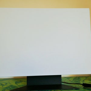 May include: A white canvas mounted on a black stand. The canvas is blank and ready for painting.