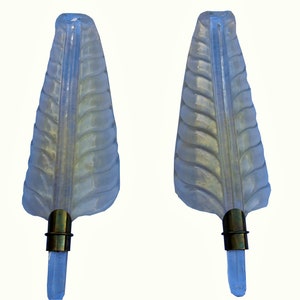 May include: Two clear, leaf-shaped wall sconces with a textured design. Each sconce has a brass-colored base and a clear, rectangular crystal-like element at the bottom. The sconces are mounted on a white background.